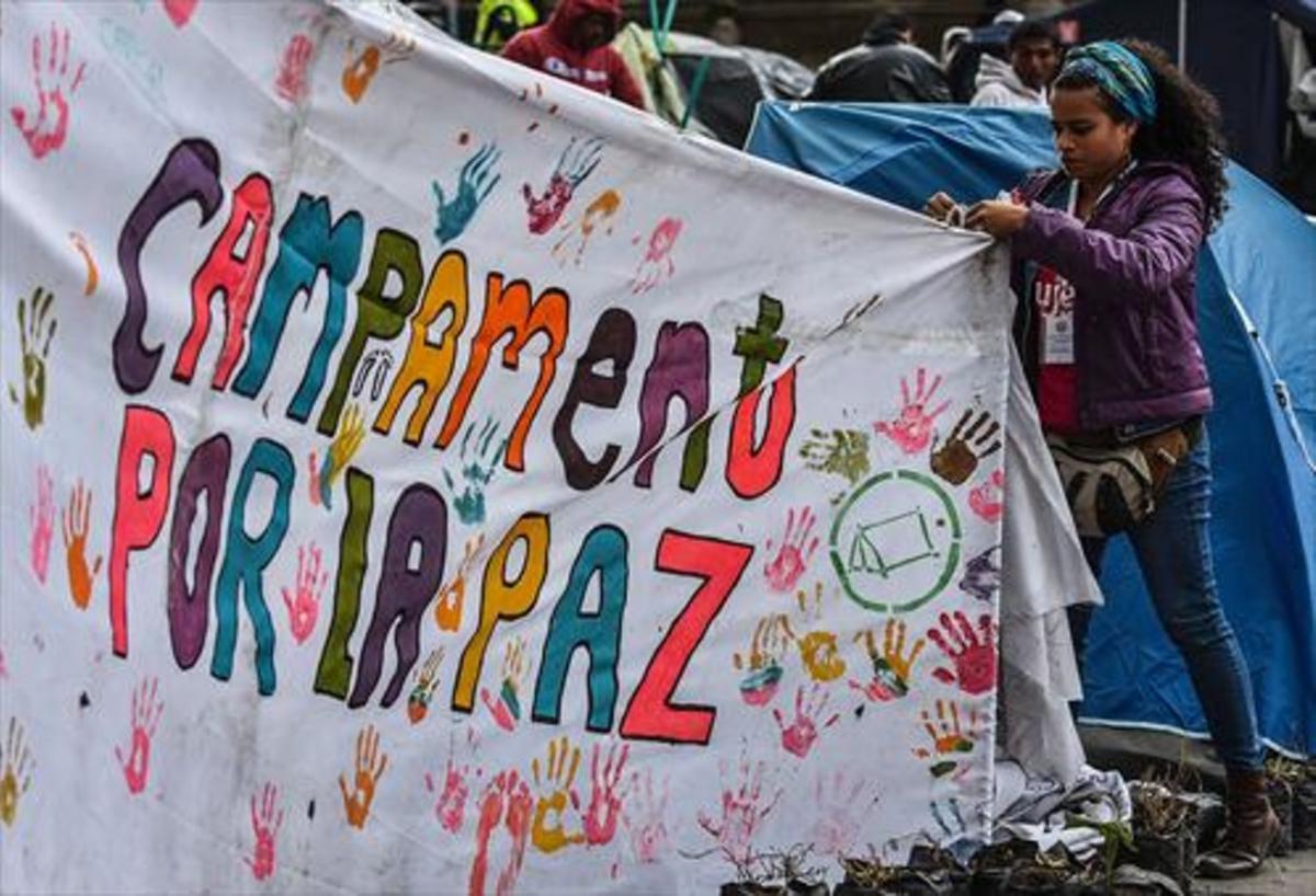 Una joven ayuda a colocar una pancarta a favor del acuerdo de paz en una acampada en Bogotá.