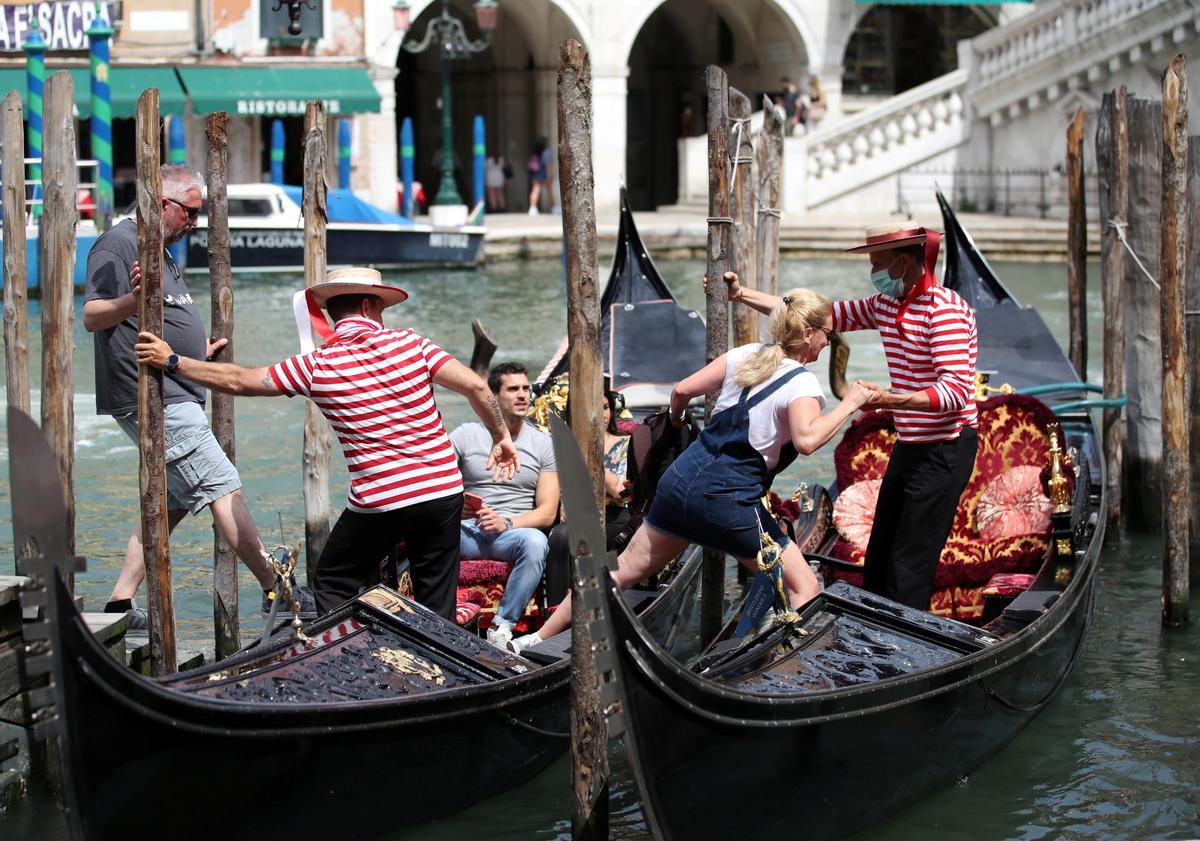 Dos gondoleros ayudan a unos turistas a subir a bordo, en Venecia.