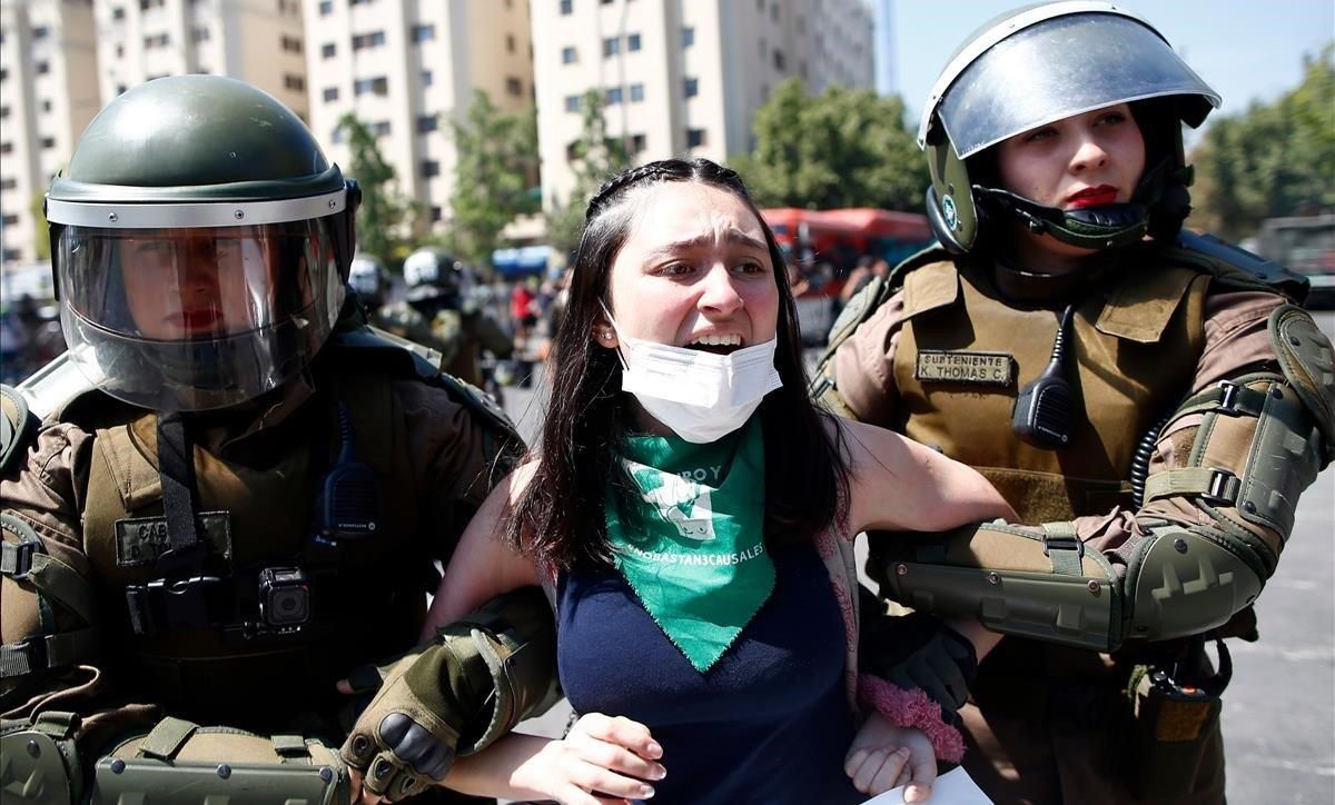 Dos agentes antidisturbios detienen a una joven manifestante en Santiago de Chile. Dos agentes antidisturbios detienen a una joven manifestante en Santiago de Chile.