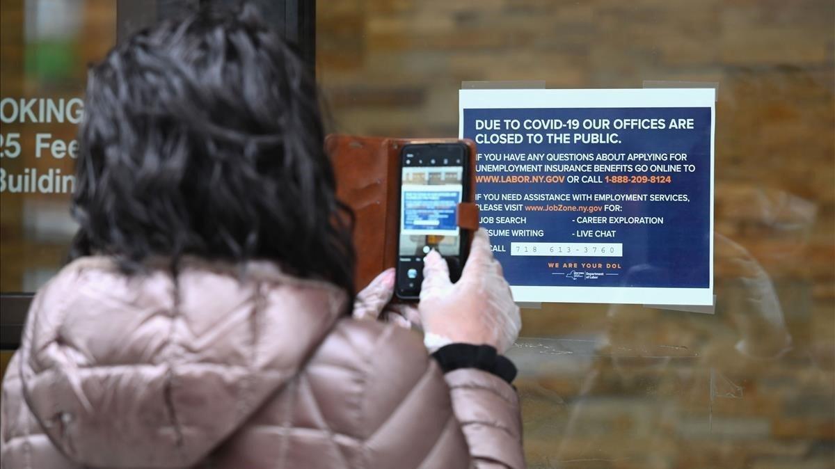 Una mujer toma una foto de un cartel colgado frente a una oficina del Departamento de Trabajo cerrada por coronavirus, este miércoles en Nueva York.