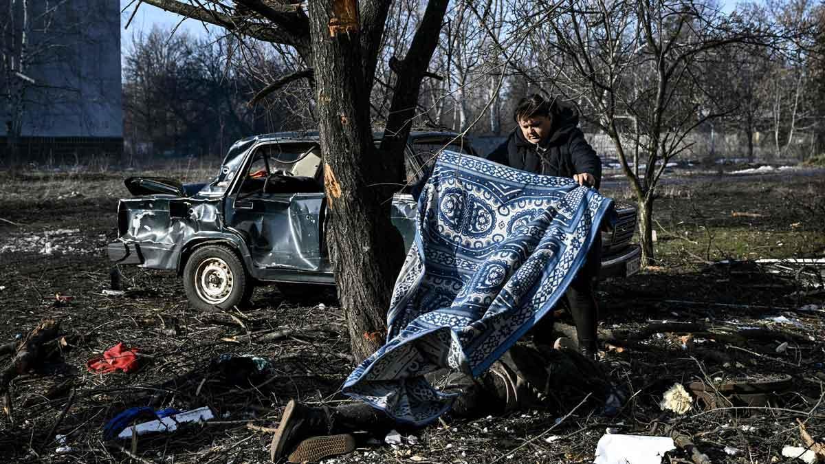 Rusia ataca Ucrania. En la foto, un hombre usa una alfombra para cubrir un cuerpo que descansa en el suelo, en la ciudad ucraniana de Chuguiv.