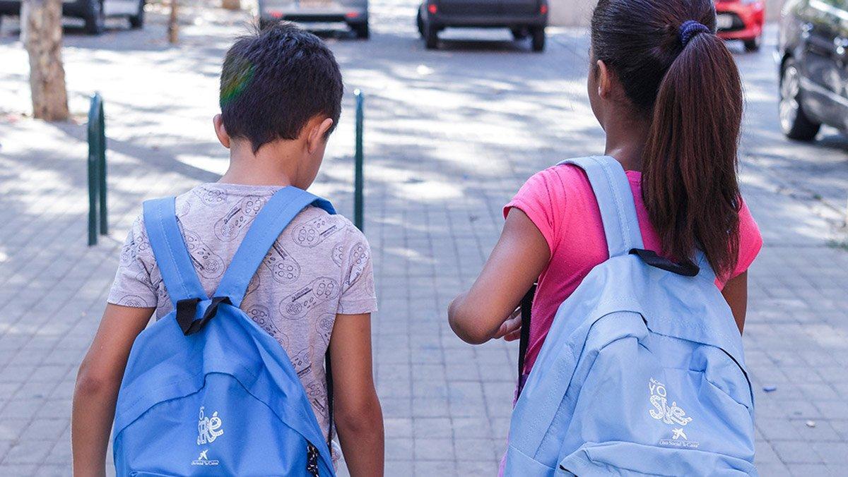 Dos niños que participan en el proyecto Chapotea, con las mochilas de CaixaProinfancia cargadas de material escolar.