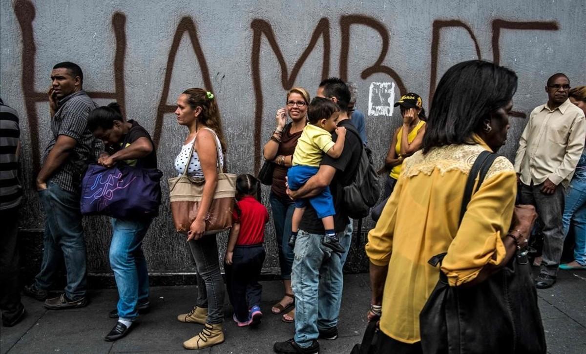 Venezolanos hacen cola frente a una pintada con la palabra ’hambre’, en Caracas. Venezolanos hacen cola frente a una pintada con la palabra ’hambre’, en Caracas.