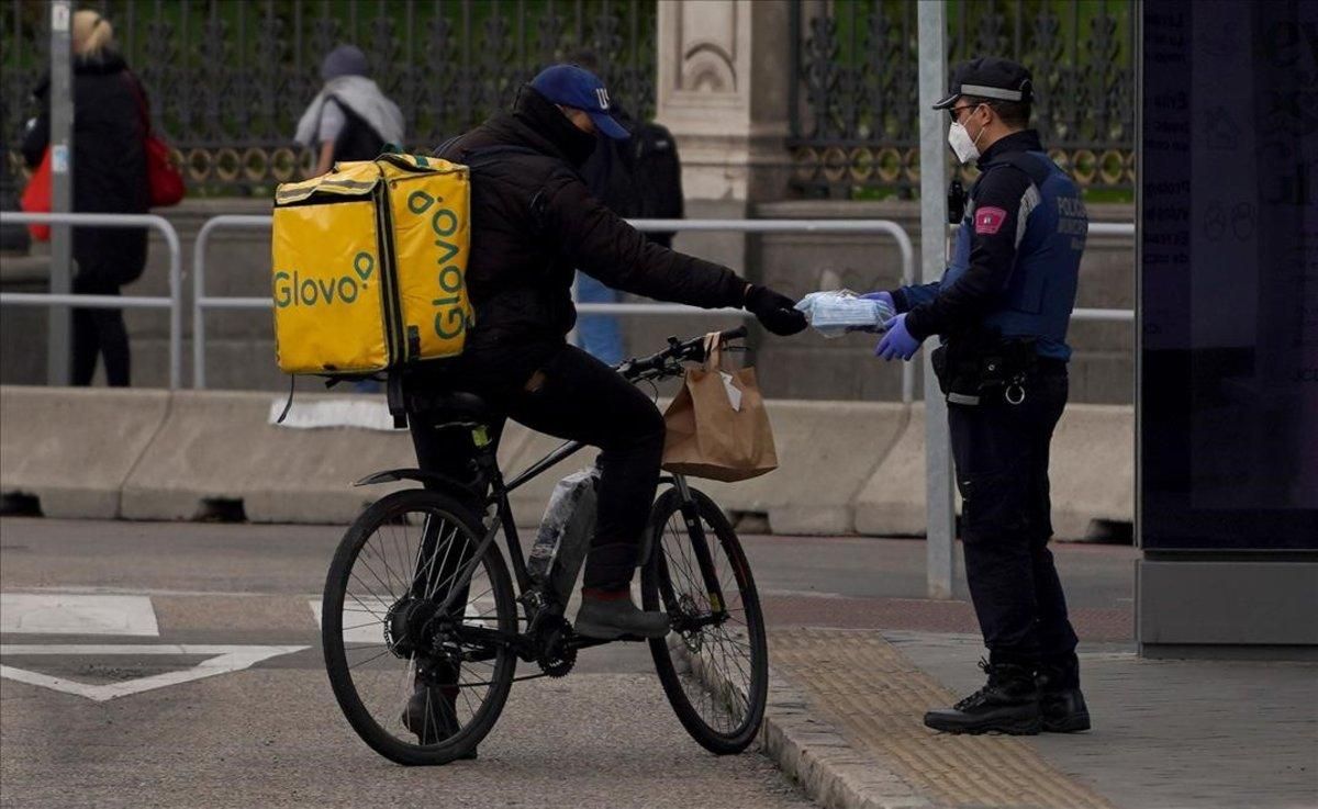Un policía entrega una mascarilla a un repartidor de Glovo. Un policía entrega una mascarilla a un repartidor de Glovo.