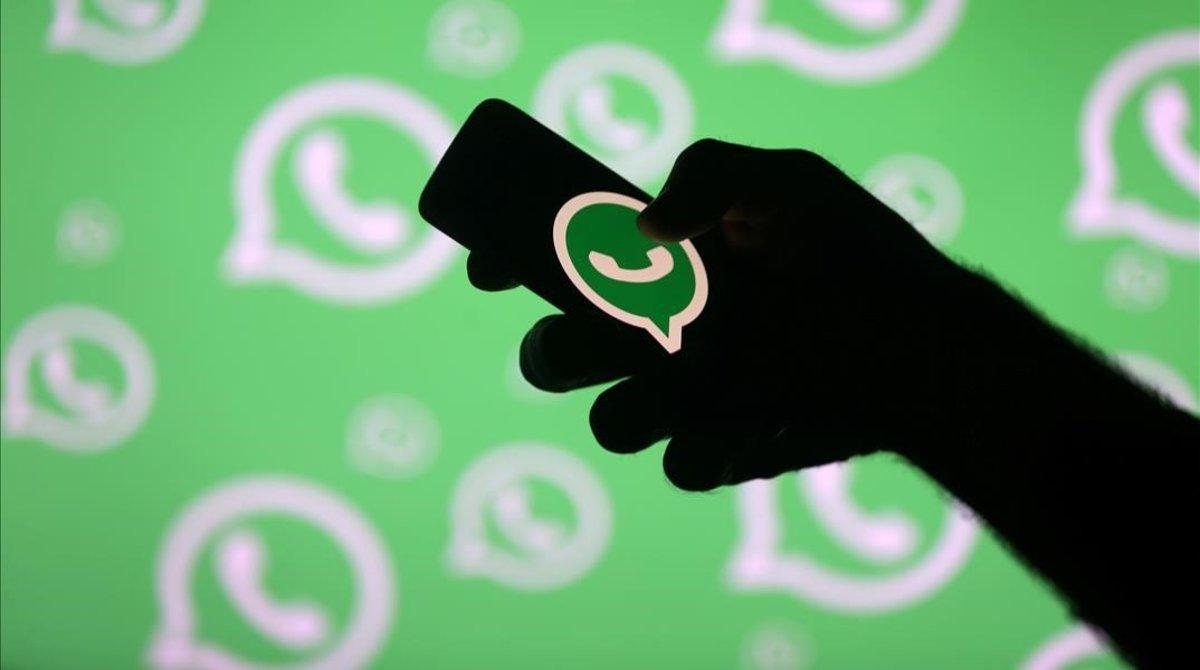 La silueta de un brazo sostiene un teléfono con el logo de WhatsApp.