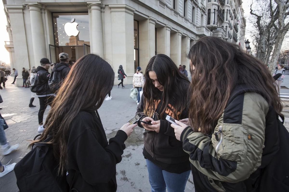 Unas jóvenes usan su smartphone delante de una tienda Apple en Barcelona.