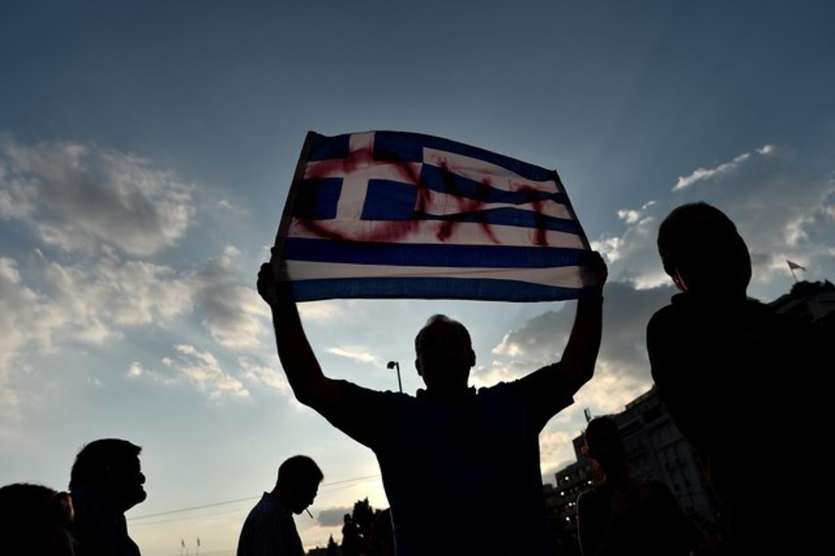 Un individuo enarbola una bandera de Grecia donde está escrito ’no’.