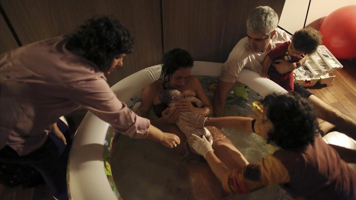 Una mujer da a luz en su casa, dentro de una piscina de agua caliente y rodeada de su familia y otros asistentes.