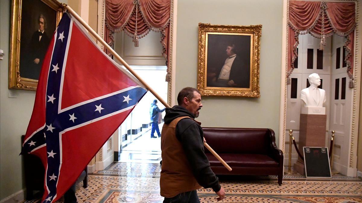 Un participante en el asalto al Capitolio de EEUU pasea por el edificio con una bandera confederada. Un participante en el asalto al Capitolio de EEUU pasea por el edificio con una bandera confederada.