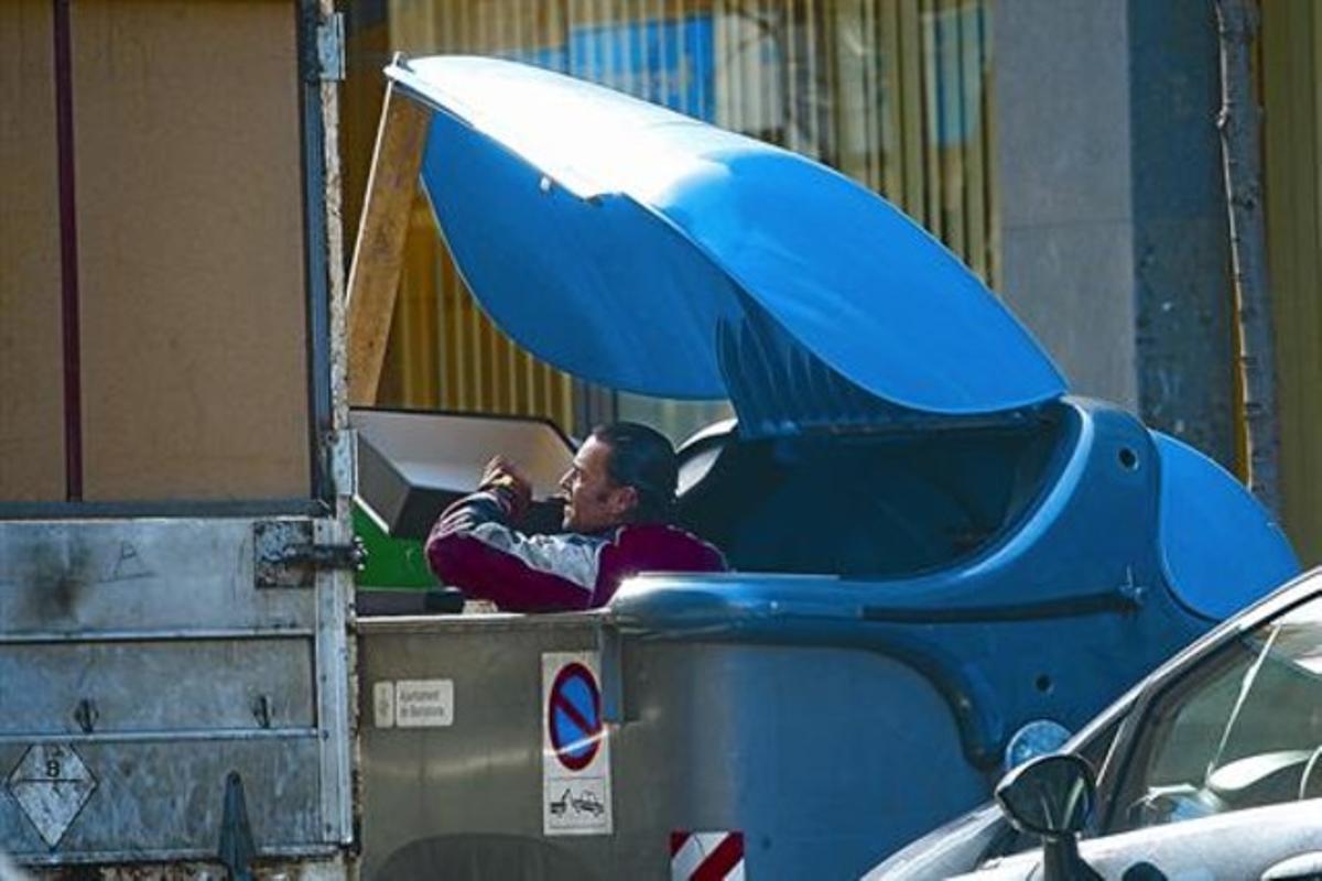 Un hombre saca cajas de cartón de un contenedor de reciclaje del Ayuntamiento de Barcelona, en febrero del 2011.