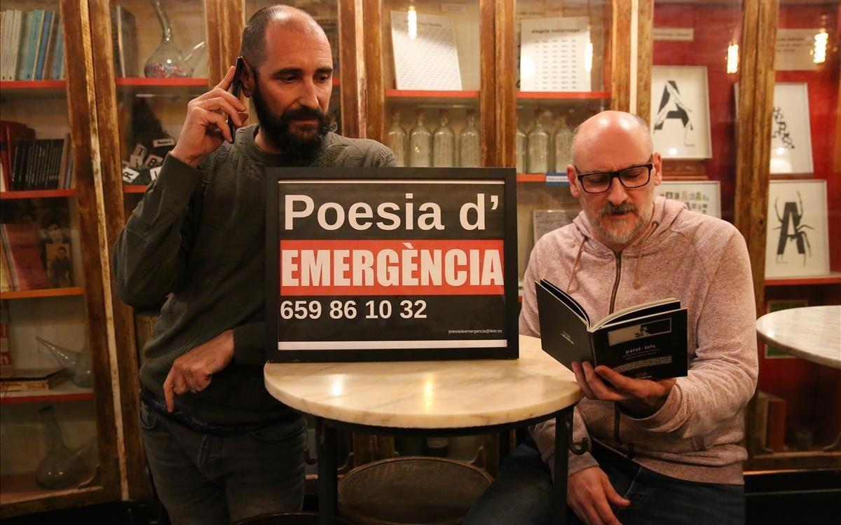 Edu Bernal y Fede Nieto posan con un cartel con el teléfono de emergencias poéticas en la entrada de  L’Horiginal. Aquí se suele intercambiar el móvil los miércoles entre voluntarios. 