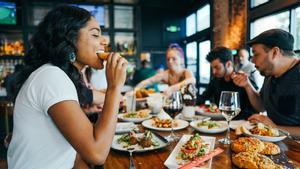 Una mujer come en una mesa de un restaurante con varias personas.