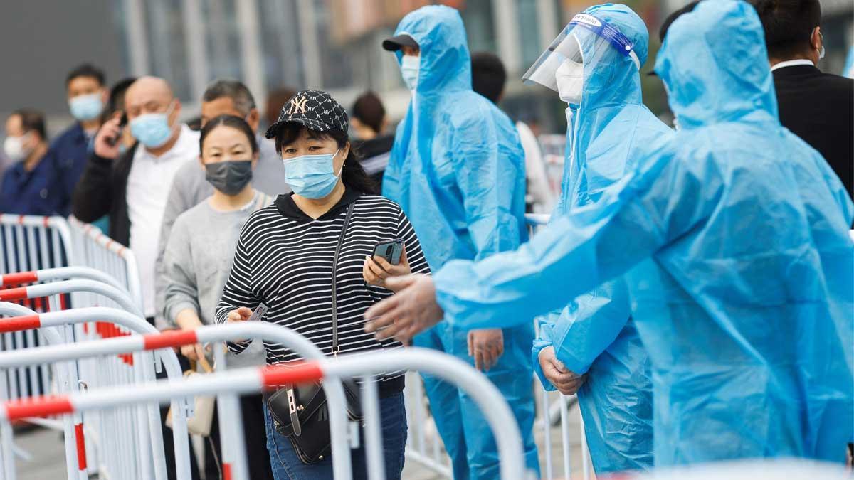 Ciudadanos de Pekín con mascarilla pasan junto a trabajadores sanitarios, en la cola para realizarse tests del coronavirus.
