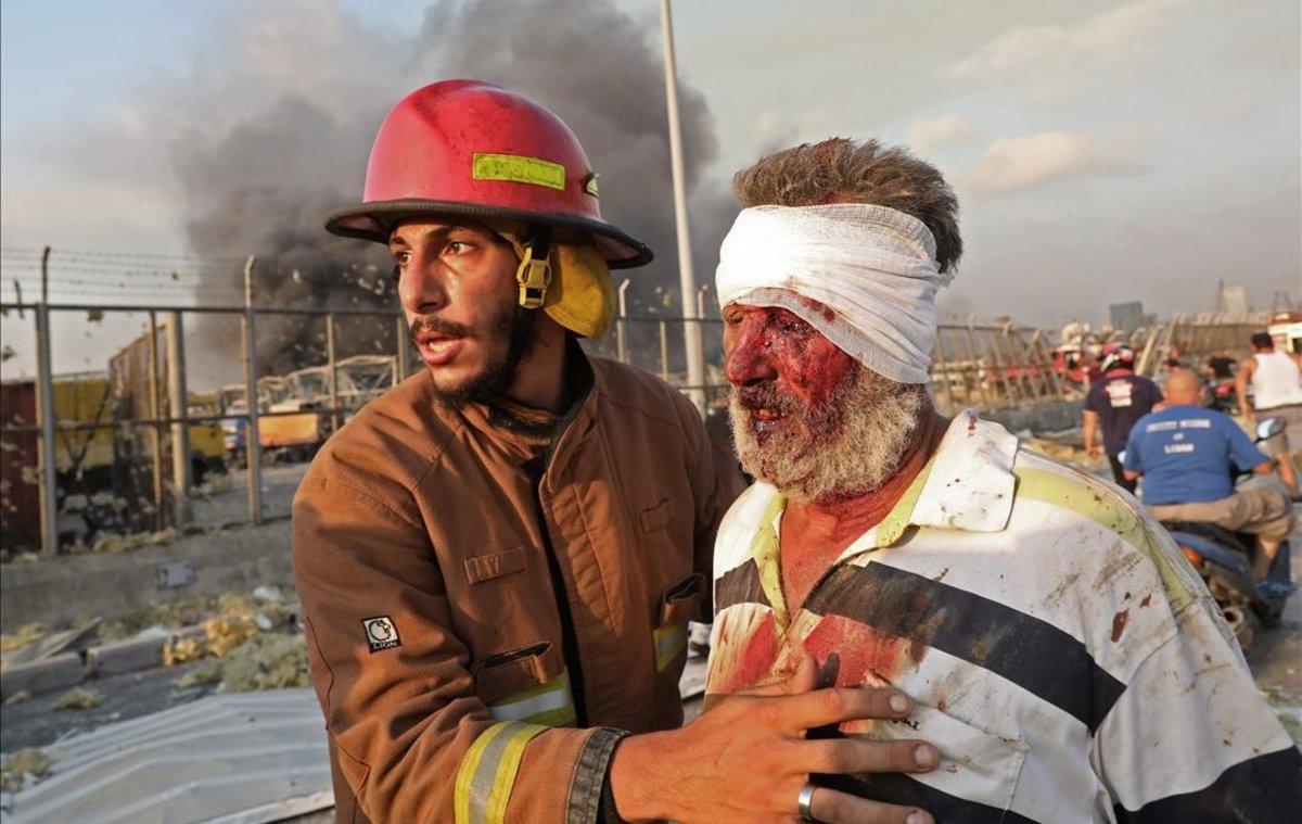 Un hombre herido es ayudado por un bombero, tras la explosión en el puerto de Beirut.