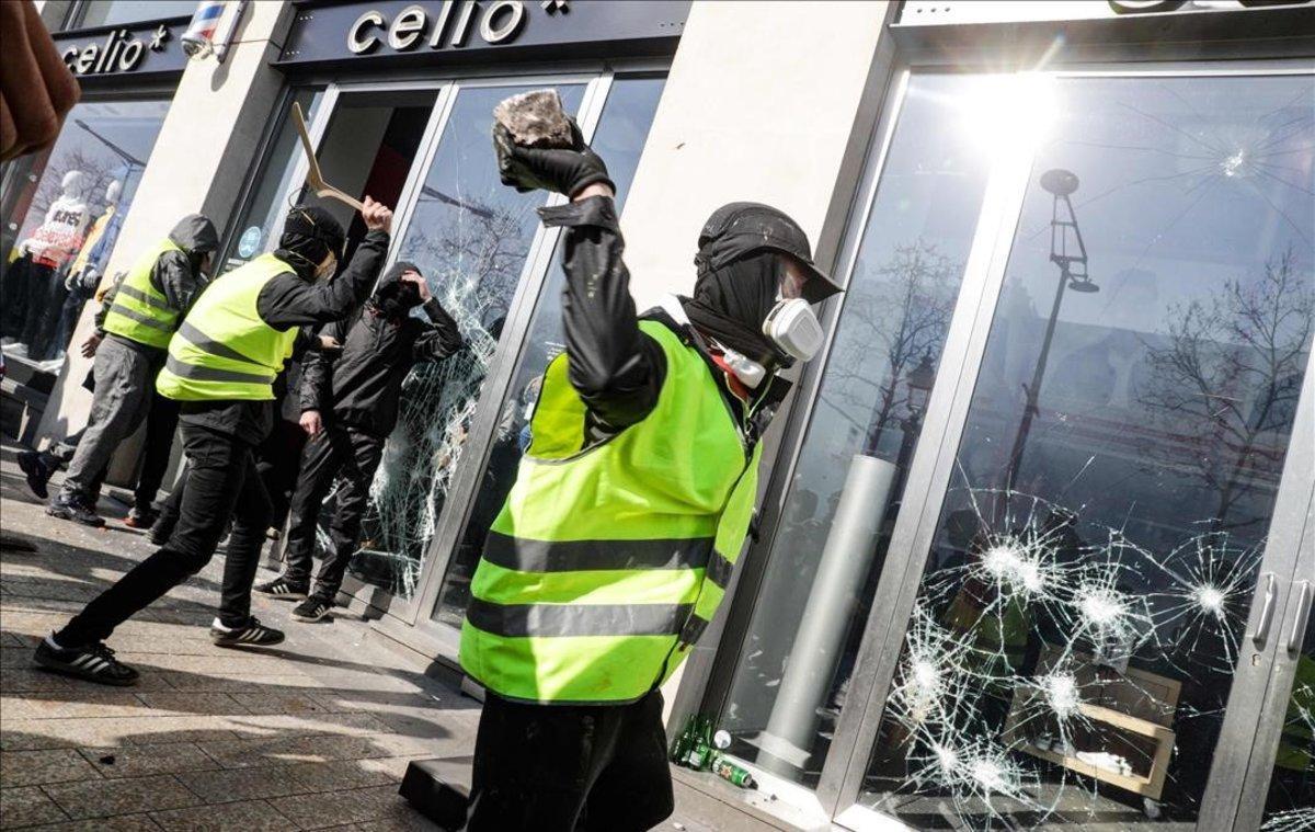 Un ’chaleco amarillo’ rompe el cristal de una tienda en los Campos Elíseos de París.