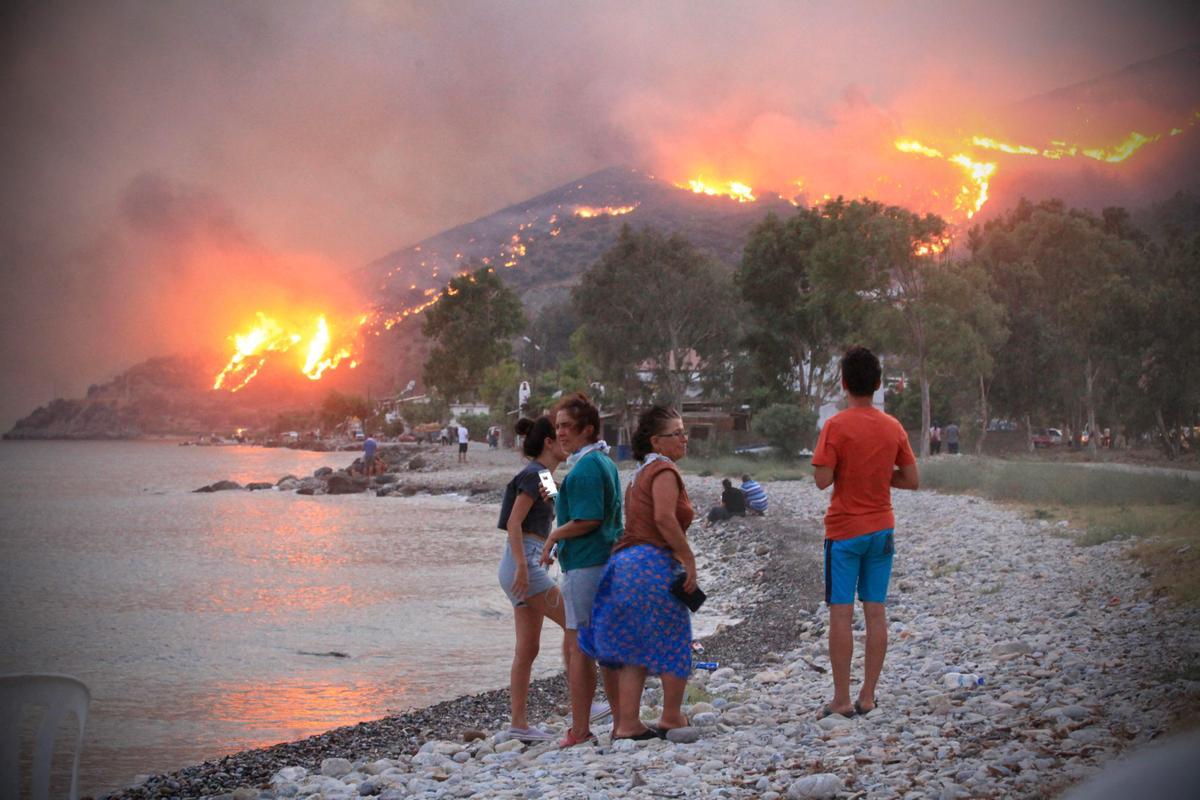 Gente en la playa observa la expansión de las llamas en la ciudad costera de Oren, en la región turca de Mugla.