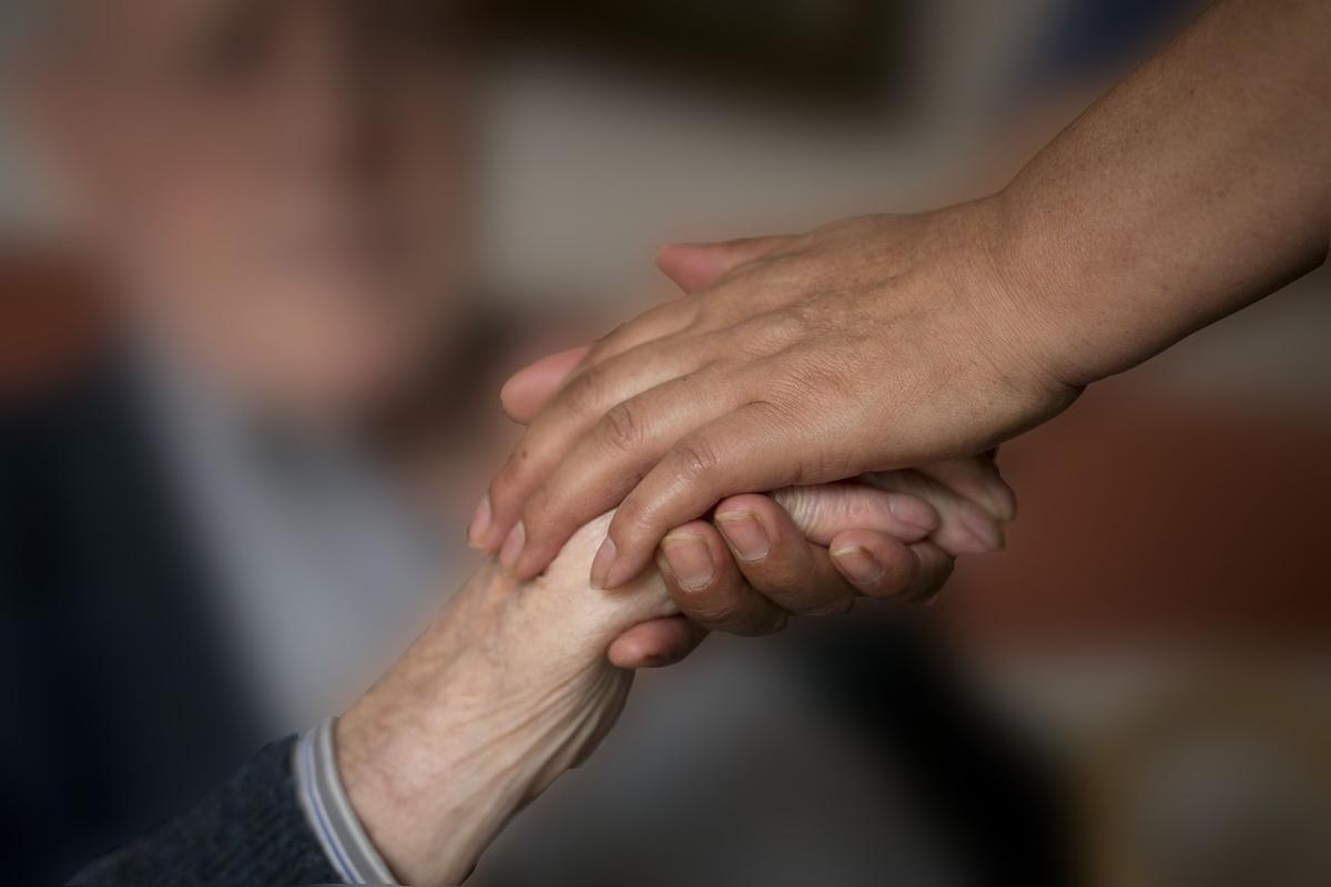 Un cuidador coge la mano de un enfermo de alzhéimer.
