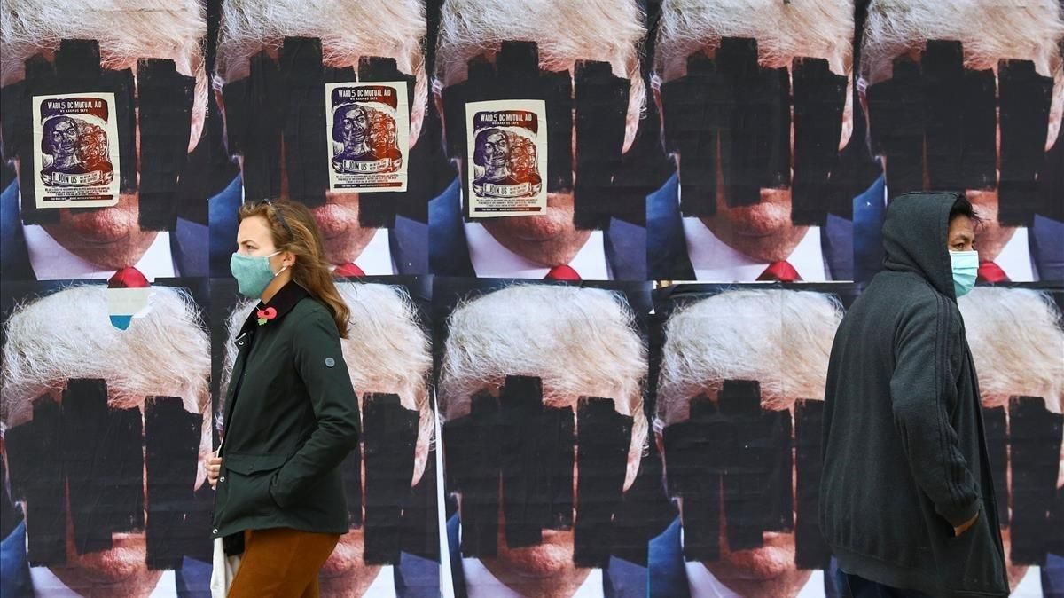 Dos personas caminan ante carteles de Donald Trump tachados, este viernes en Washington. Dos personas caminan ante carteles de Donald Trump tachados, este viernes en Washington.