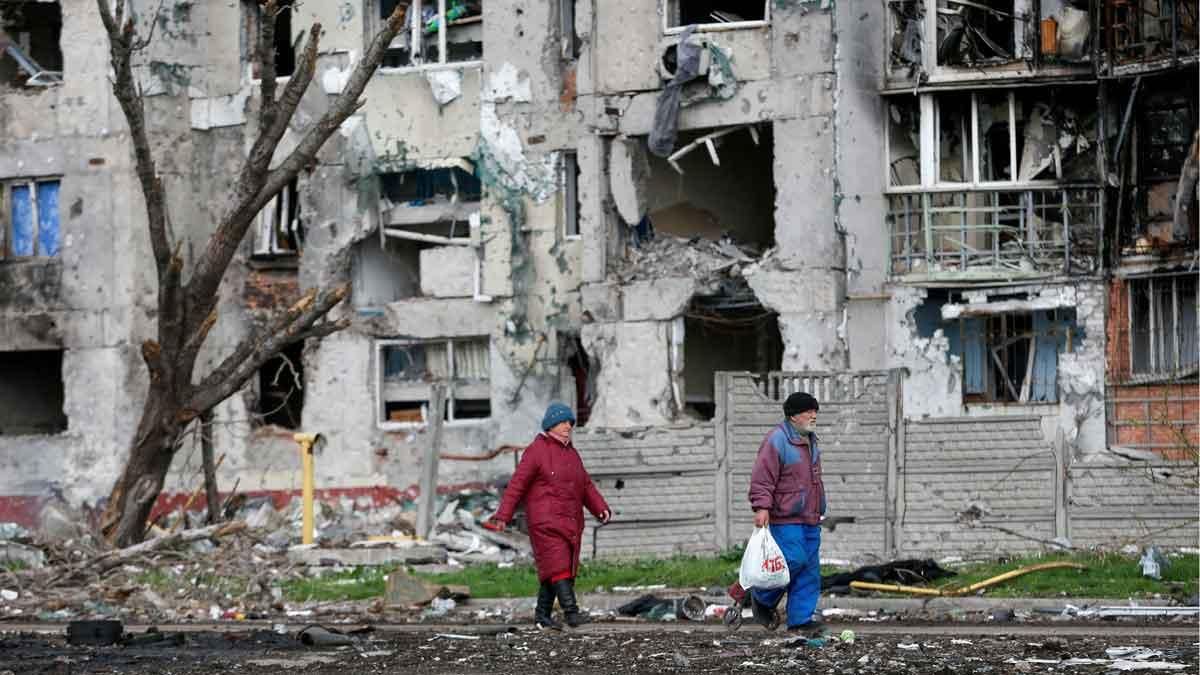Dos personas pasan junto a un edificio de casas destruido, en la ciudad de Mariúpol. Dos personas pasan junto a un edificio de casas destruido, en la ciudad de Mariúpol.