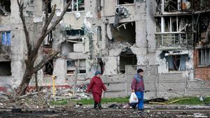 Dos personas pasan junto a un edificio de casas destruido, en la ciudad de Mariúpol.