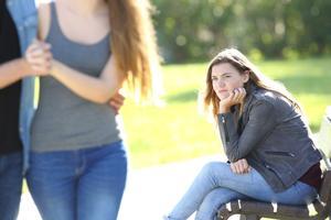 Una chica sentada en el parque siente envidia al ver a una pareja.