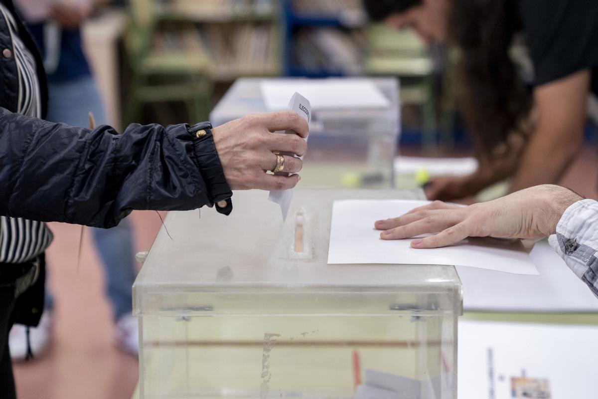 Una persona mete su voto en la urna en un colegio electoral.