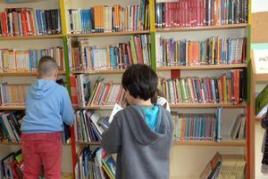 Tres alumnos de primaria consultan libros en una biblioteca escolar. 