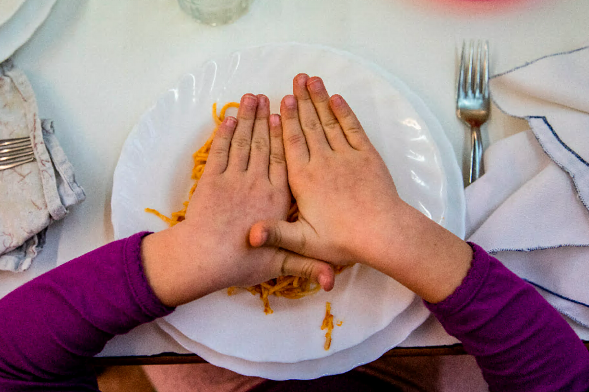 Un niño tapa con las manos su plato de pasta. Un niño tapa con las manos su plato de pasta.