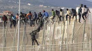 Un policía trata de hacer bajar a uno de los inmigrantes encaramados a la valla de Melilla.