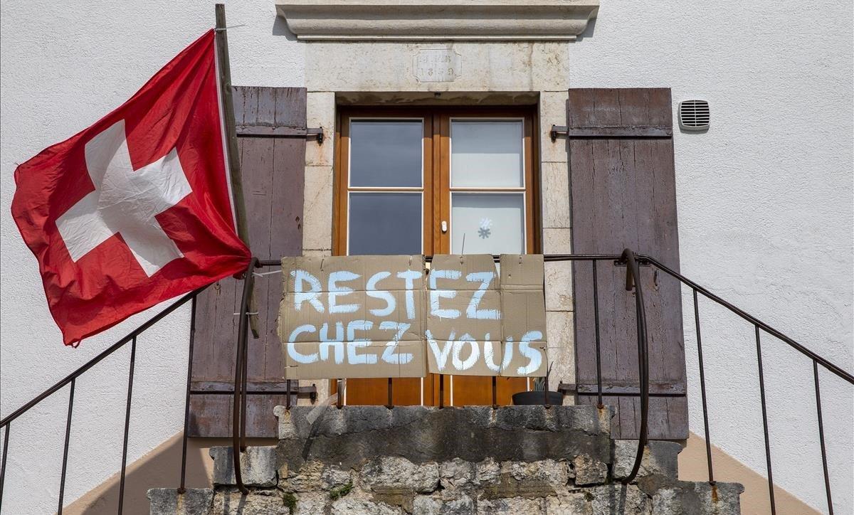 Un ciudadano de Ginebra cuelga un letrero en francés pidiendo que la gente se quede en casa.