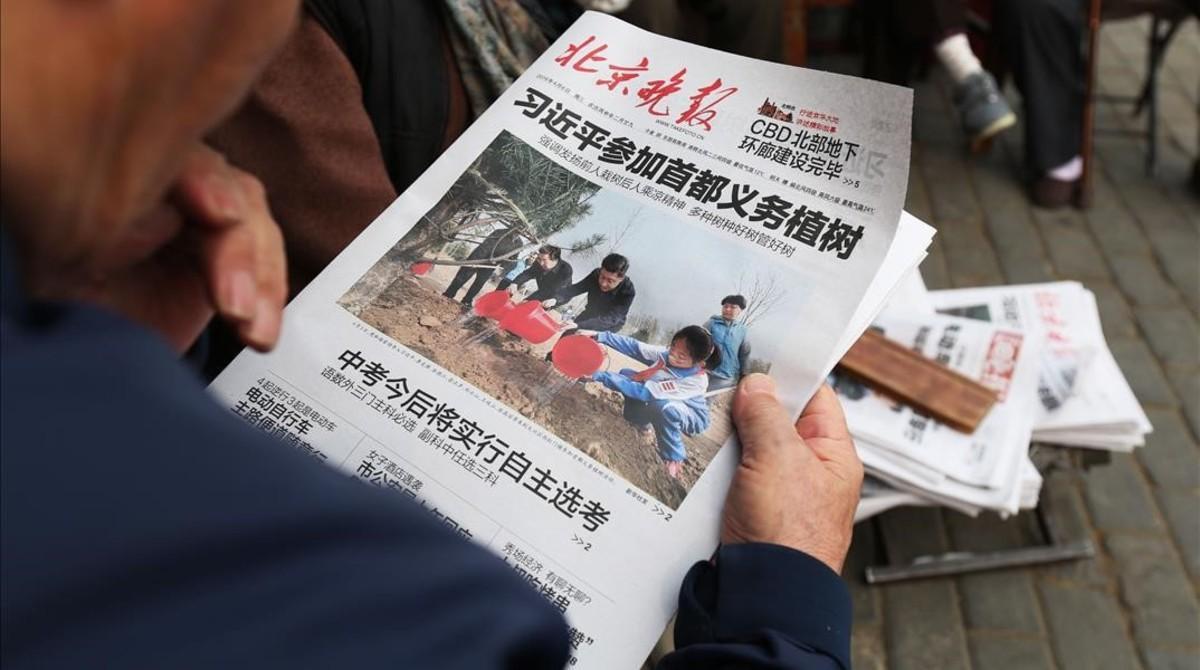 Un hombre lee un periódico donde aparece en portada el presidente Xi en una plantación de árboles, el 6 de abril, en Pekín.