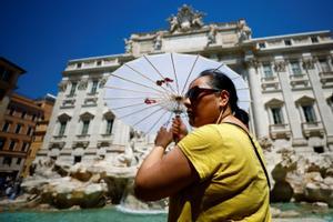 Una mujer se refugia del sol bajo un paraguas en la fuente de Trevi durante el clima cálido cuando una ola de calor golpea Europa en Roma, Italia.