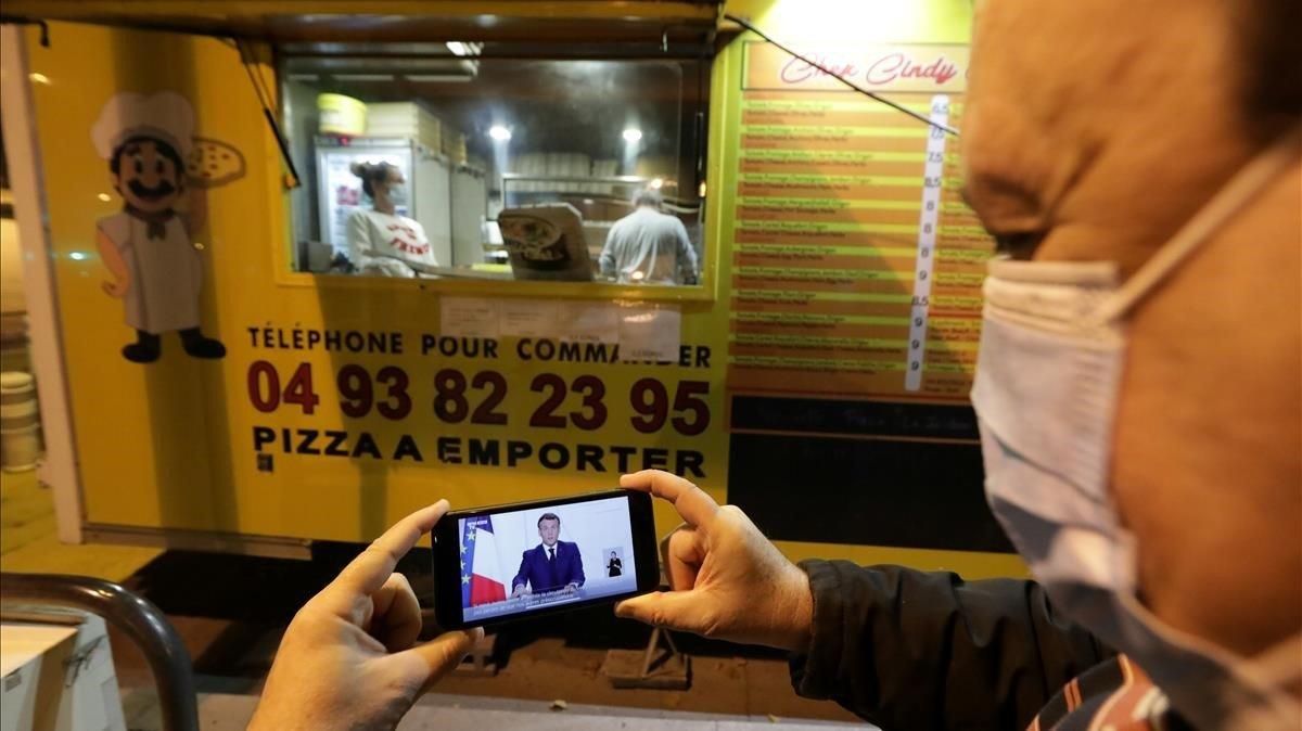 Un hombre mira el discurso de Macron a través de su móvil junto a un local que vende pizzas para llevar. Un hombre mira el discurso de Macron a través de su móvil junto a un local que vende pizzas para llevar.