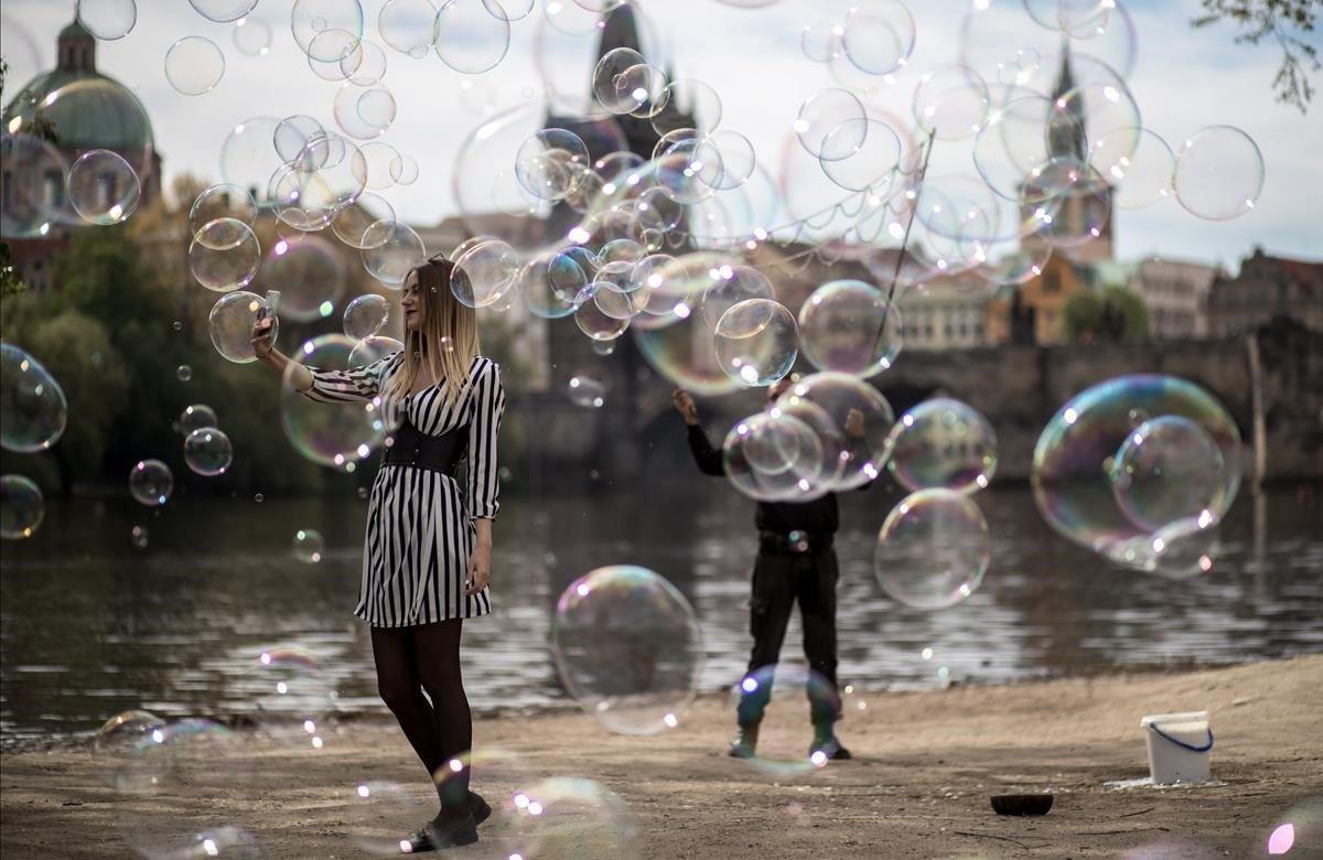 Una chica se hace un selfi rodeada de las burbujas que hace flotar en el aire un artista callejero a orillas del río Moldava, este viernes, en Praga, República Checa.