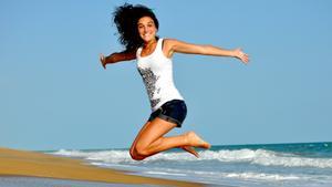 Una mujer salta sonriendo en una playa, feliz