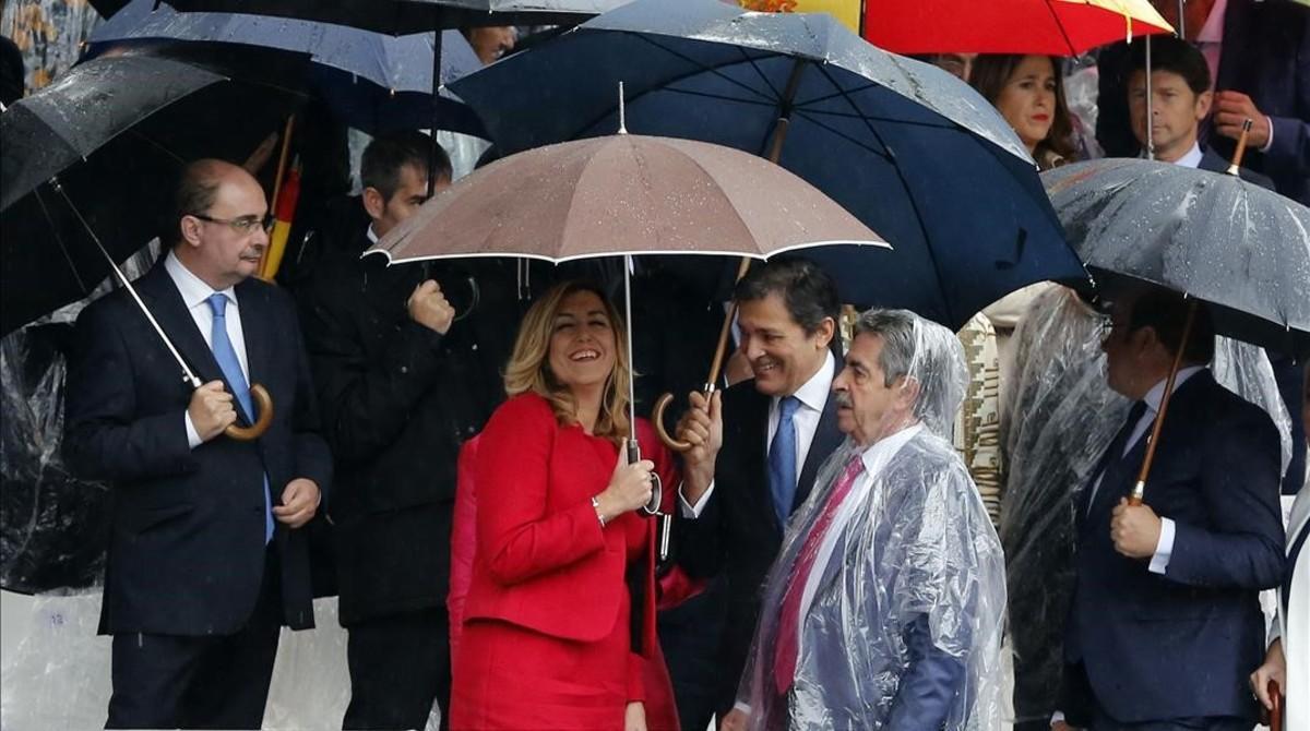 Miguel Ángel Revilla, con chubasquero, junto a Susana Díaz y Javier Fernández en el desfile del día de la Hispanidad.