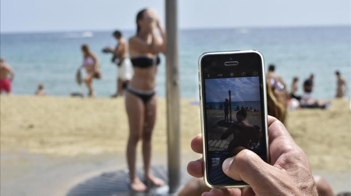 Una mujer se ducha en la playa de Barcelona delante de la cámara de un teléfono móvil. 