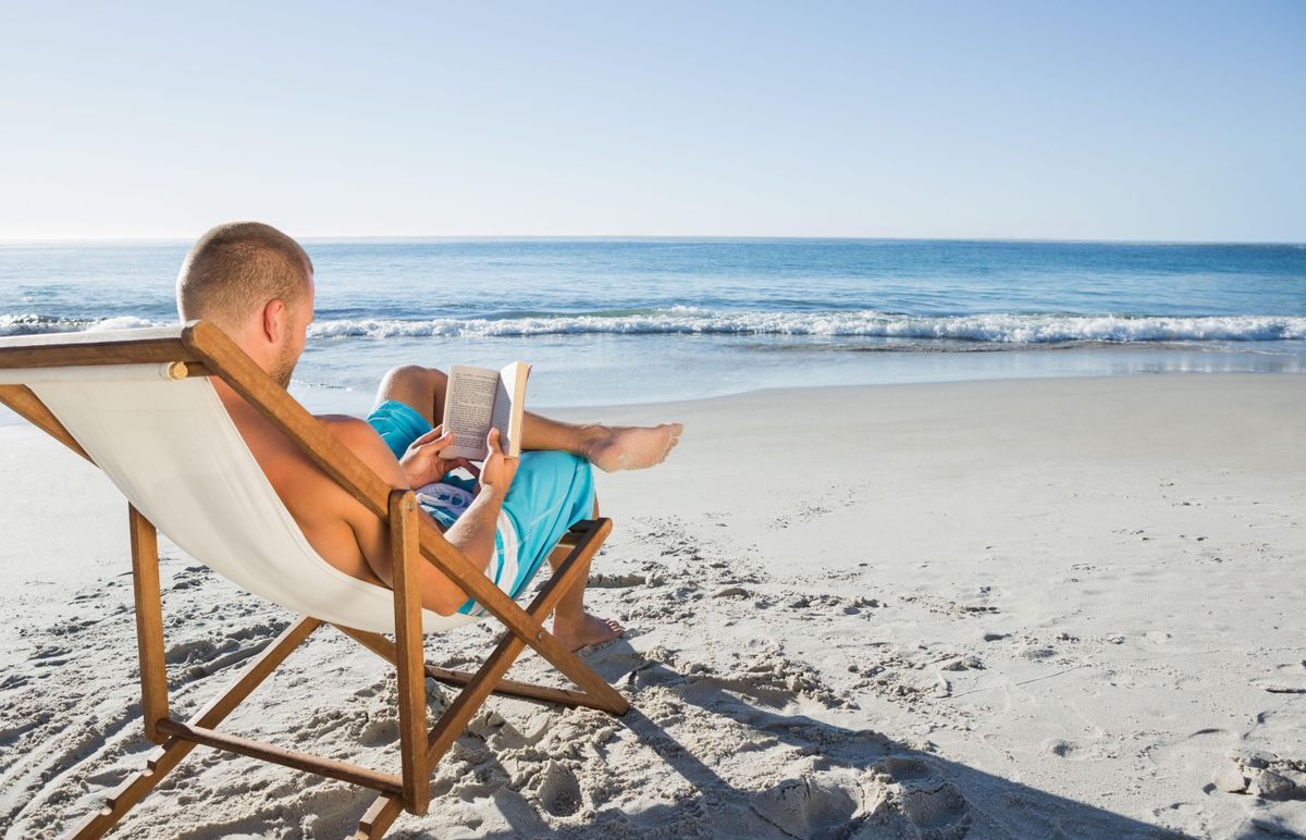 Un hombre leyendo un libro en la playa. Un hombre leyendo un libro en la playa.