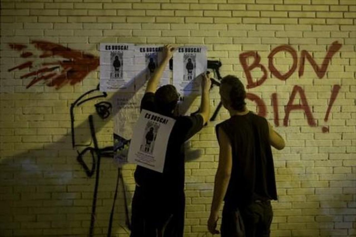 Dos chicos cuelgan carteles denunciando la retirada por parte de los Mossos del decorado de las fiestas. Dos chicos cuelgan carteles denunciando la retirada por parte de los Mossos del decorado de las fiestas.