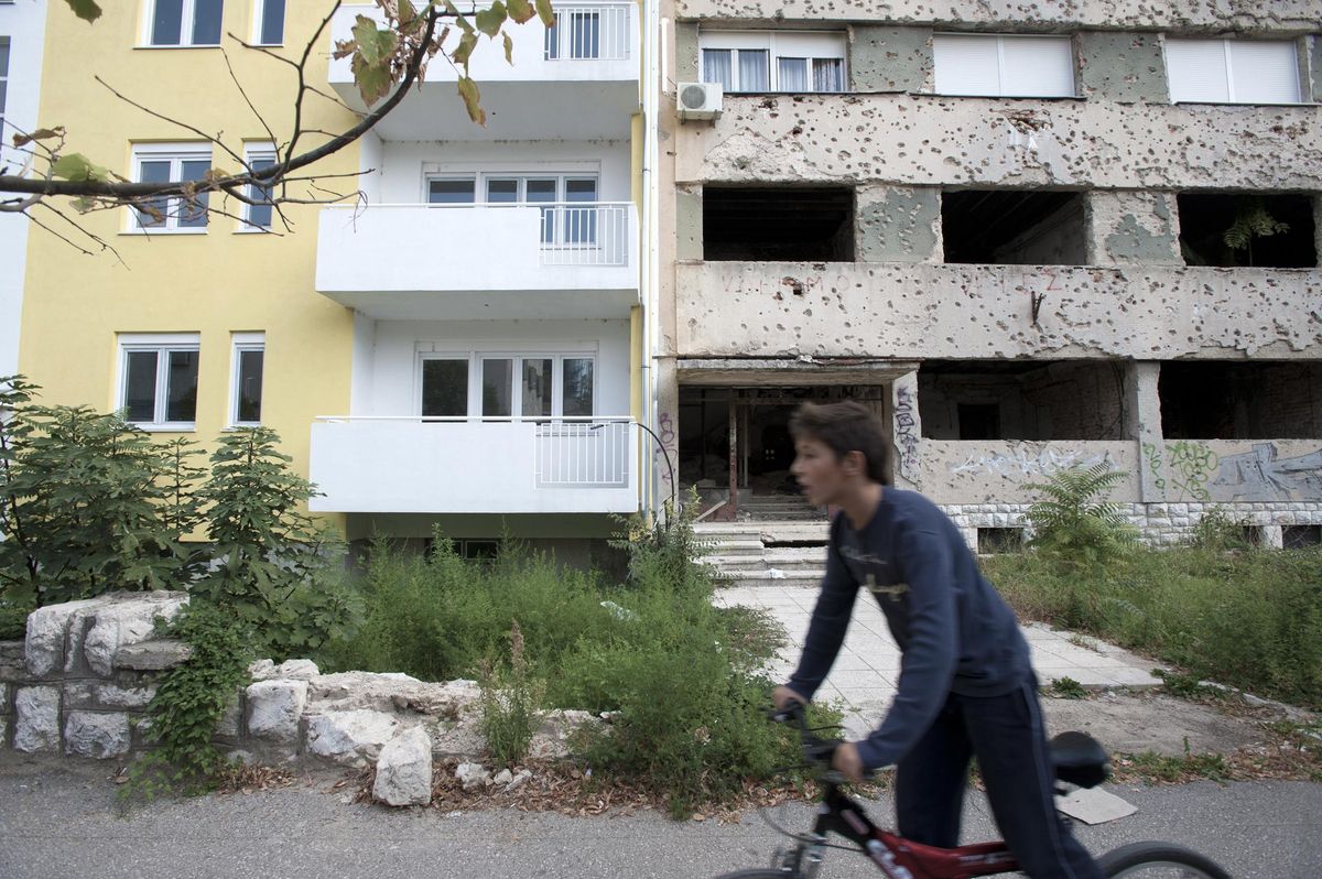 Un chico pasa en bicicleta frente a edificios nuevos y edificios con marcas de la guerra en Bosnia en el año 2013. Un chico pasa en bicicleta frente a edificios nuevos y edificios con marcas de la guerra en Bosnia en el año 2013.
