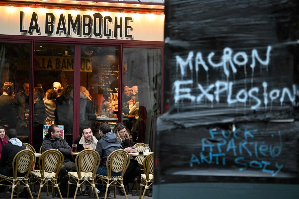 Una terraza de un bar de París junto a una pintada en la que se puede leer Macron explosión, este sábado, un día después de que el Consejo Constitucional diera su aval a la reforma de las pensiones.