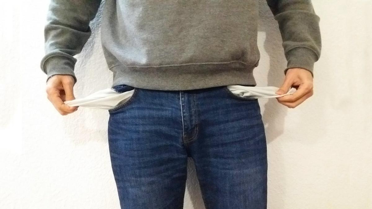 Un hombre muestra sus bolsillos del pantalón, los cuales están vacíos.