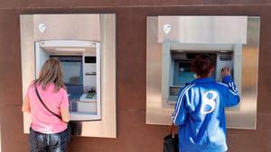 Dos personas sacan dinero de sendos cajeros automáticos en Madrid.