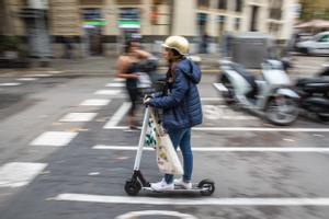 Una usuaria de patinete eléctrico, con casco, por las calles de Barcelona