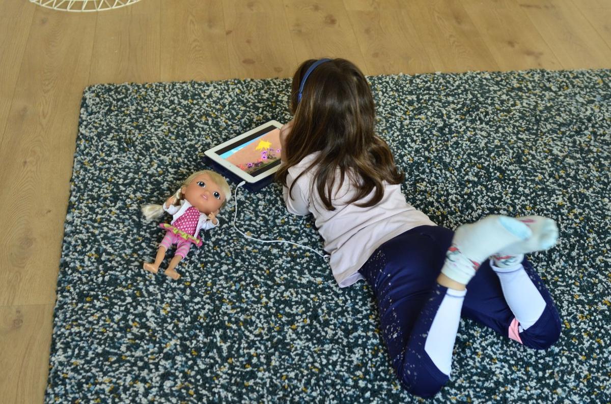 Una niña se entretiene en casa con una tablet y muñecas.