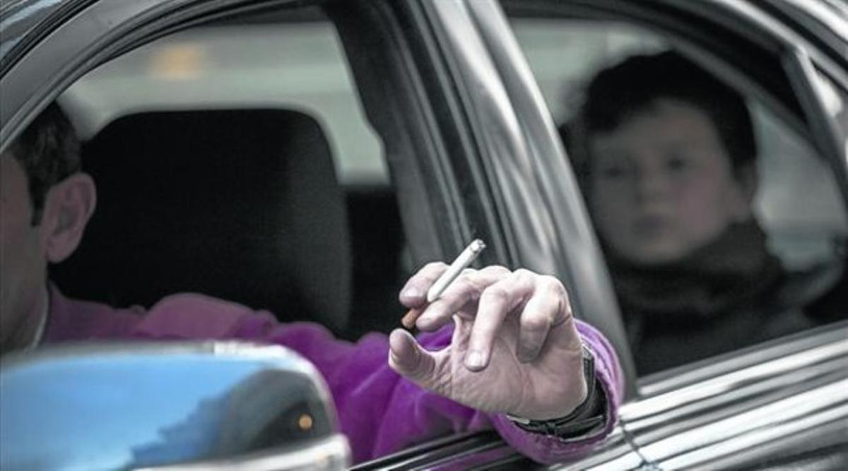 Un hombre fuma mientras conduce un coche en el que viaja con un niño. Un hombre fuma mientras conduce un coche en el que viaja con un niño.