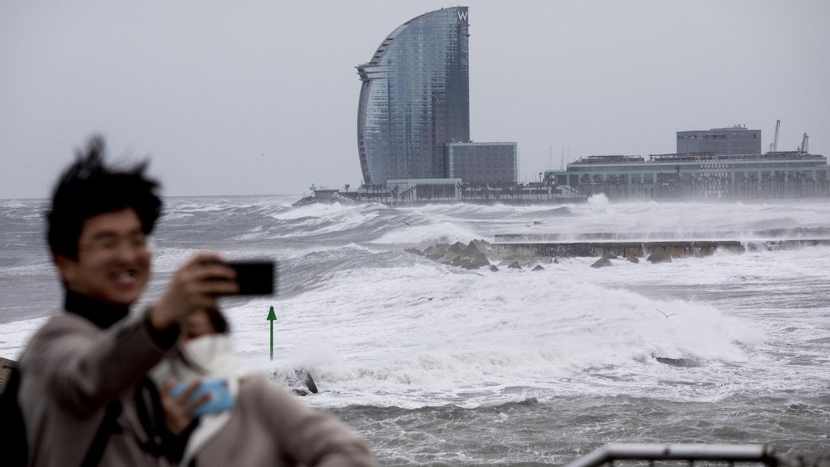 Un par de turistas se hacen una foto con el oleaje del temporal Glòria sobre Barcelona, en enero de 2020 Un par de turistas se hacen una foto con el oleaje del temporal Glòria sobre Barcelona, en enero de 2020