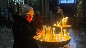 Una mujer enciende una vela en una iglesia en Leópolis, Ucrania, junto a otras personas que rezan.