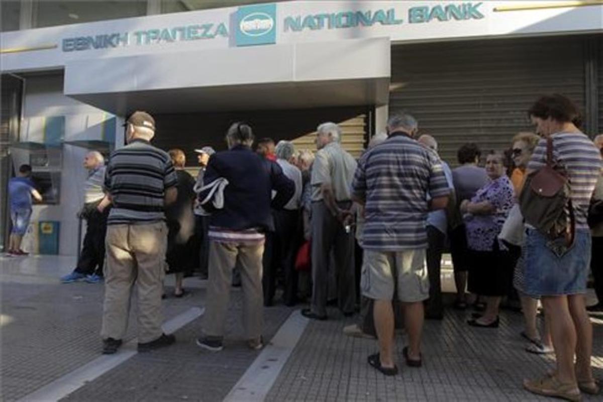Ciudadanos griegos haciendo cola para sacar el mínimo de efectivo permitido, ante una sucursal del Banco Nacional de Grecia hoy lunes tras imponerse el corralito.