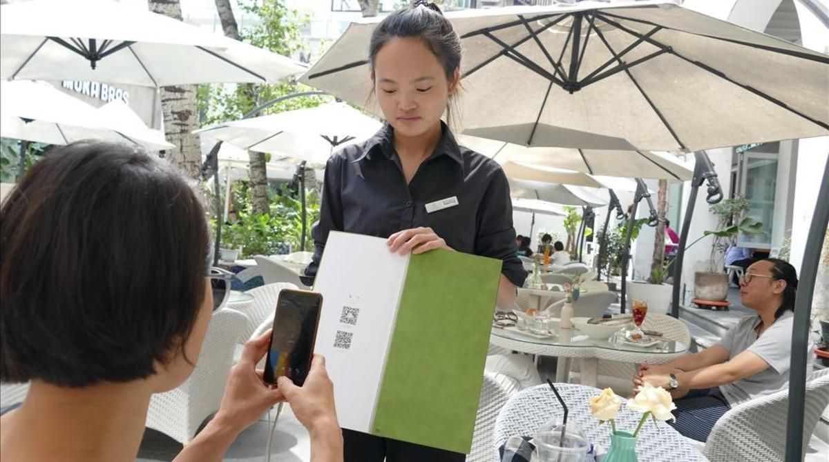 Una joven paga su consumición en un terraza de Shanghái con el teléfono móvil. Una joven paga su consumición en un terraza de Shanghái con el teléfono móvil.